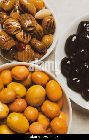 Ein Set aus drei Olivensorten in weißen Schüsseln - ganze große grüne Oliven, schwarze Oliven, grüne, in Öl gegrillte Oliven, entsteint, Draufsicht, Nahaufnahme, fragm Stockfoto