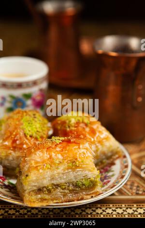 Stillleben mit heißem orientalischem Kaffee, in Zezve gebrüht. Auf dem arabischen Tisch befindet sich eine kleine Kaffeetasse und köstliches Honigbaklava mit Pistazien auf einer Untertasse Stockfoto