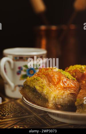 Stillleben mit heißem orientalischem Kaffee, in Zezve gebrüht. Auf dem arabischen Tisch befindet sich eine kleine Kaffeetasse und köstliches Honigbaklava mit Pistazien auf einer Untertasse Stockfoto