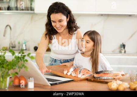 Glückliche Mutter und Tochter bereiten Lachs in der Küche vor Stockfoto