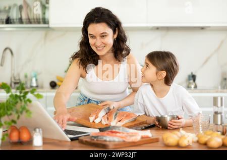 Glückliche Mutter und Tochter bereiten Lachs in der Küche vor Stockfoto