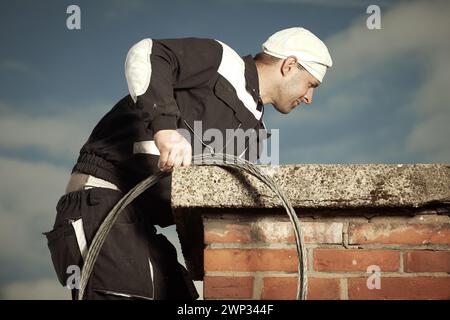 Schornsteinfeger Mann in der Arbeit Uniform Reinigung Ziegelsteinschornstein auf dem Dach des Gebäudes Stockfoto