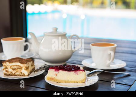 Nachmittagstee mit heißem Tee und leckeren Kuchen auf dem Tisch und im Swimmingpool. Hotelresort oder Ruhekonzept Stockfoto