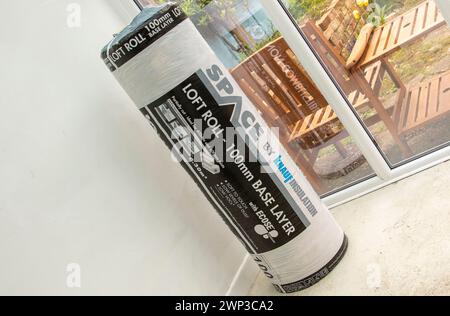 Unbenutzte Rolle mit 100 mm Grundschicht Knauf Loft-Isolierung in Kunststoffverpackung, die an einem Ende in der Ecke eines Wintergartens steht. Stockfoto