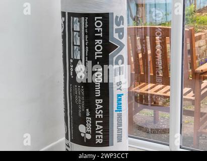 Unbenutzte Rolle mit 100 mm Grundschicht Knauf Loft-Isolierung in Kunststoffverpackung, die an einem Ende in der Ecke eines Wintergartens steht. Stockfoto