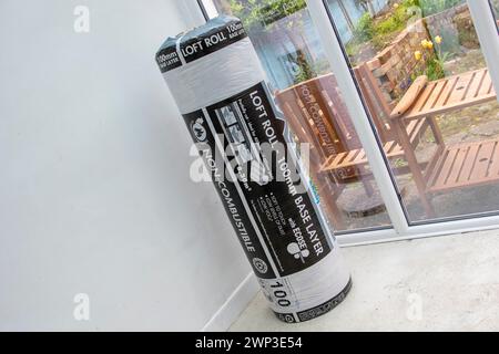 Unbenutzte Rolle mit 100 mm Grundschicht Knauf Loft-Isolierung in Kunststoffverpackung, die an einem Ende in der Ecke eines Wintergartens steht. Stockfoto