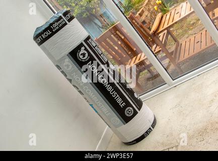 Unbenutzte Rolle mit 100 mm Grundschicht Knauf Loft-Isolierung in Kunststoffverpackung, die an einem Ende in der Ecke eines Wintergartens steht. Stockfoto