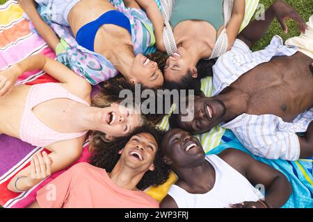 Verschiedene Freunde lachen zusammen, während sie draußen auf einer bunten Decke liegen Stockfoto