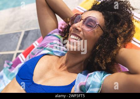 Frau mit rosa Sonnenbrille und blauem Badeanzug genießt die Sonne am Pool Stockfoto