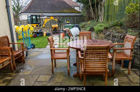 Bauarbeiten mit einem kleinen Bagger und Baumaterialien in der Einfahrt mit Gartenmöbeln, Schottland, Großbritannien Stockfoto