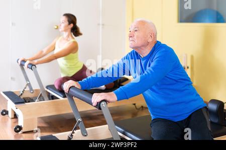 Älterer Mann, der Stretching-Übungen auf Pilates Reformer macht Stockfoto