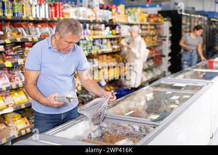 Ein alter Käufer wählt gefrorenen Fisch in einem großen Supermarkt Stockfoto