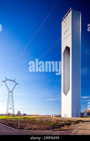 Hochspannungsleitungen, die neben einer hochaufragenden Solaranlage unter blauem Himmel verlaufen. Stockfoto