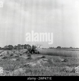 1950er Jahre, historische, Bauern auf einem Traktor und Ballenpresse auf dem Feld, die kleine Heuballen herstellen, England, Großbritannien. Stockfoto