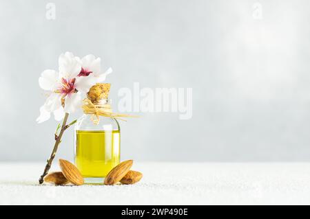 Glasflasche Mandelöl und Mandelnüsse, Mandeln mit Mandelblüten auf dem Tisch. Mandelhintergrundkonzept mit Kopierraum Stockfoto