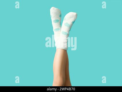 Beine einer jungen Frau in warmweißen gepunkteten Socken auf blauem Hintergrund Stockfoto