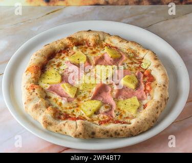 Tropische hawaiianische Pizza mit Ananasscheiben und Schinken auf gebackener Teigbasis serviert im Ganzen mit Copyspace, Pizza Stockfoto