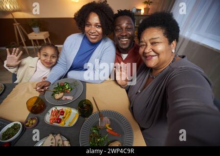 Porträt einer großen afroamerikanischen Familie, die gemeinsam Selfie am Esstisch macht und mit Oma in der Hand winkt Stockfoto