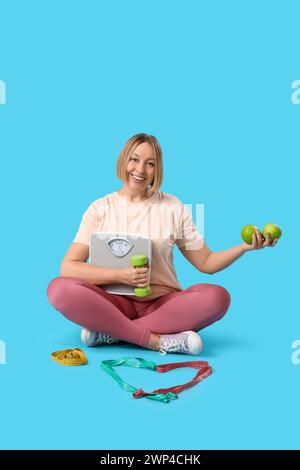 Hübsche junge Frau mit Maßband, Äpfeln und Hantel auf blauem Hintergrund. Gewichtsverlust-Konzept Stockfoto