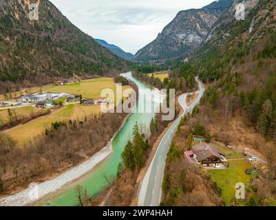 Blick auf einen Fluss mit einer Straße, die durch ein grünes Waldgebiet führt, umgeben von Bergen und bewölktem Himmel, Bad Reichenhall, Saalach, Bayern, Deutschland Stockfoto