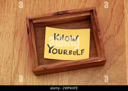 Ein Stück gelbes Papier mit dem Satz "Know Yourself" drauf in einer kleinen leeren Holzkiste. Nahaufnahme. Stockfoto