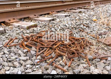 Ein Haufen rostiger Eisenbahnspitzen auf zerquetschtem Stein neben den Gleisen. Stockfoto