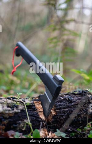 Vertikales Porträt in diesem eindrucksvollen Bild stehen stolz ein Bushcraft und eine Überlebensaxt, fest eingebettet in einen Baumstamm auf dem Waldboden. Dieses essen Stockfoto