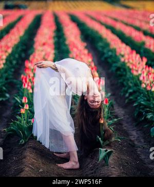 Langhaarige Brünette, die sich im weiten Tulpenfeld rückwärts beugt Stockfoto