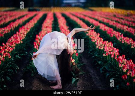 Langhaarige Brünette, die sich im weiten Tulpenfeld rückwärts beugt Stockfoto