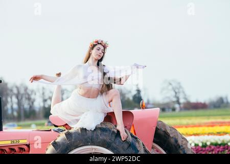 Frau, die sich auf dem Traktor abspaltet und auf einem riesigen Tulpenfeld steht Stockfoto