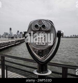 Ein Münzteleskop zeigte zum Wasser hin, wobei die Freiheitsstatue und die Skyline von Manhattan in der Ferne sichtbar waren. Stockfoto