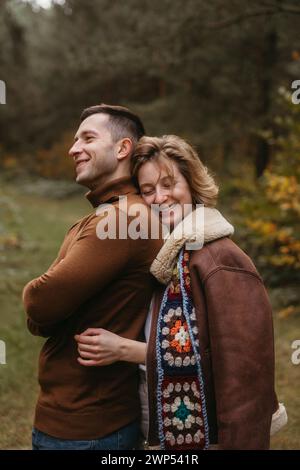 Lächelnde weiße Frau umarmt einen Mann von hinten, glückliches Paar, das Zeit im Herbstpark draußen verbringt Stockfoto