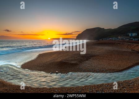 Seatown, Dorset, Großbritannien. März 2024. Wetter in Großbritannien. Der Fluss Winniford fließt bei Sonnenuntergang in Seatown an der Dorset Jurassic Coast über den Strand und blickt auf die Klippen von Golden Cap, während der Himmel nach einem Morgen des Regens klar wird. Bildnachweis: Graham Hunt/Alamy Live News Stockfoto