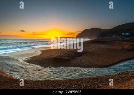 Seatown, Dorset, Großbritannien. März 2024. Wetter in Großbritannien. Der Fluss Winniford fließt bei Sonnenuntergang in Seatown an der Dorset Jurassic Coast über den Strand und blickt auf die Klippen von Golden Cap, während der Himmel nach einem Morgen des Regens klar wird. Bildnachweis: Graham Hunt/Alamy Live News Stockfoto