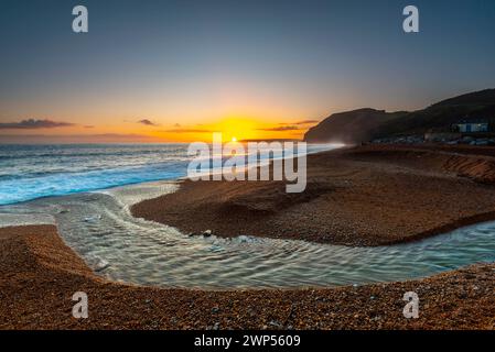 Seatown, Dorset, Großbritannien. März 2024. Wetter in Großbritannien. Der Fluss Winniford fließt bei Sonnenuntergang in Seatown an der Dorset Jurassic Coast über den Strand und blickt auf die Klippen von Golden Cap, während der Himmel nach einem Morgen des Regens klar wird. Bildnachweis: Graham Hunt/Alamy Live News Stockfoto