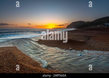 Seatown, Dorset, Großbritannien. März 2024. Wetter in Großbritannien. Der Fluss Winniford fließt bei Sonnenuntergang in Seatown an der Dorset Jurassic Coast über den Strand und blickt auf die Klippen von Golden Cap, während der Himmel nach einem Morgen des Regens klar wird. Bildnachweis: Graham Hunt/Alamy Live News Stockfoto