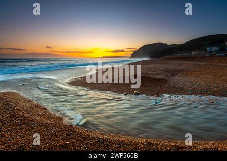 Seatown, Dorset, Großbritannien. März 2024. Wetter in Großbritannien. Der Fluss Winniford fließt bei Sonnenuntergang in Seatown an der Dorset Jurassic Coast über den Strand und blickt auf die Klippen von Golden Cap, während der Himmel nach einem Morgen des Regens klar wird. Bildnachweis: Graham Hunt/Alamy Live News Stockfoto