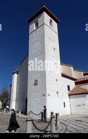 Die Kirche San Nicolás, Granada: Die reinen Linien des weißen Turms ragen wie ein Minarett in einen tiefblauen Himmel. Eine Frau geht mit einer Burka vorbei. Stockfoto