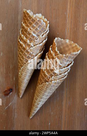 Zwei knusprige, goldbraune Waffelkegel stehen aufrecht auf einem Holztisch und können mit köstlichem Eis gefüllt werden Stockfoto
