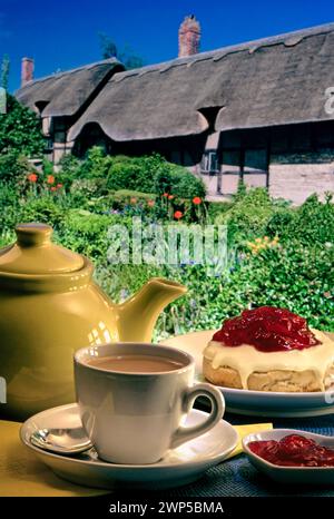 Englischer Creme-Tee, traditioneller Retro-Vintage-Stil im Freien Devon Teestube Garten Urlaub im Freien Terrasse, mit traditionellem englischem Reetgedecktem Cottage und Sommergarten im Hintergrund. England Großbritannien Stockfoto