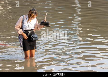 SAMUT PRAKAN, THAILAND, 11. Februar 2024, Eine lächelnde Frau waten durch eine überflutete Straße Stockfoto