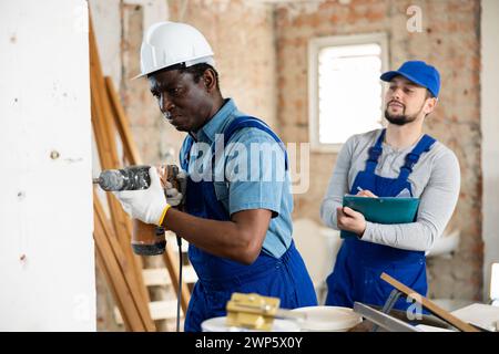 Foreman teilt dem Baumeister mit, wo er Löcher mit dem Bohrhammer bohren soll Stockfoto