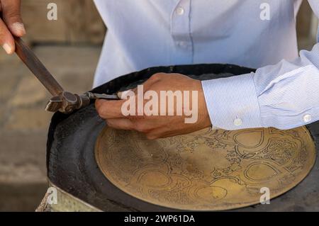 27. JUNI 2023, BUCHARA, USBEKISTAN: Der Meister, der die Metallarbeiten für den Verkauf als Souvenir macht Stockfoto