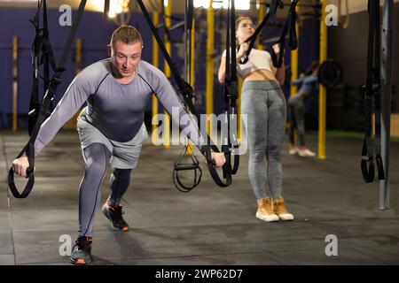 Erwachsener männlicher Athlet mit Gruppe, die an Gymnastikringen im Crossfit-Fitnessstudio trainieren Stockfoto