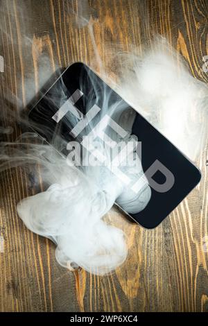 Nahaufnahme des Smartphones mit Rauchgeräuschen und Worten auf einem Holzschreibtisch. Beschädigte Ausrüstung. Stockfoto