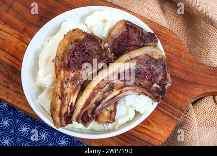 Drei Lammrippkoteletts mit Pap- oder Maismehl auf rustikalem Schneidebrett und traditionellem südafrikanischem Stoff mit Kopierraum Stockfoto