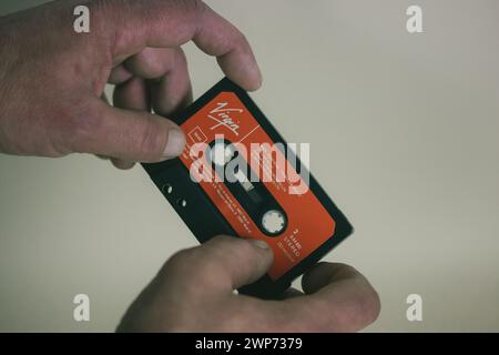 Madrid, Spanien. 2. Januar 2024 alte rote Vintage-Kassette für Kassettenrekorder, Player in Männerhand. Nostalgie für 90er, 00er Jahre Jungfrau Label Musik hören Stockfoto