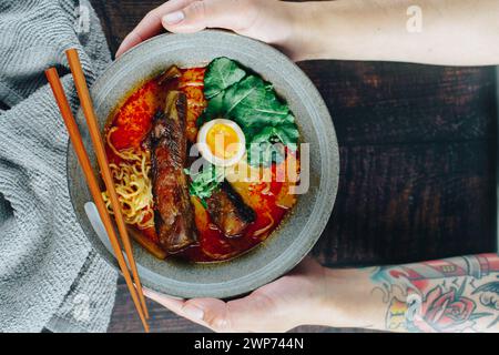 Eine Person hält eine Schüssel Ramen mit Stäbchen. Die Schüssel ist mit Nudeln, Fleisch und Gemüse gefüllt. Die Stäbchen werden in die Schüssel, Rea, gelegt Stockfoto