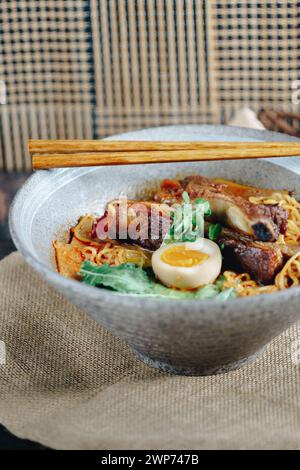 Eine Schüssel Ramen mit Fleisch und Ei darin. Die Schüssel steht auf einem Tisch mit Stäbchen daneben Stockfoto