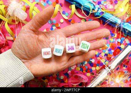 FOTOMONTAGE, Würfel mit der Aufschrift Frohes neues Jahr 2024 auf einer Hand umgeben von Konfetti und Glücksbringern, Symbolfoto Neujahr 2024 Stockfoto